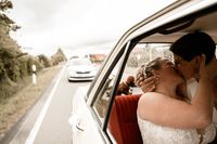 Hochzeitsfotografie: Blick aus dem Beifahrerfenster, Brautpaar kuesst sich im Auto